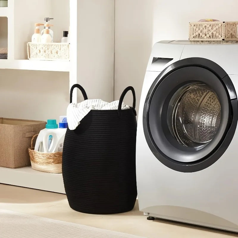 Black Boho Cotton Rope Storage Basket with clothes next to a washing machine in a laundry room.