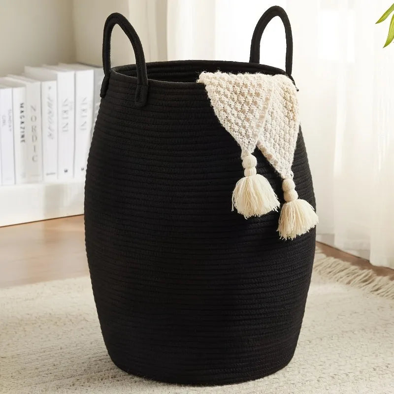 Black Boho Cotton Rope Storage Basket  with handles and a white textured tassel draped over it, on a light wooden floor.