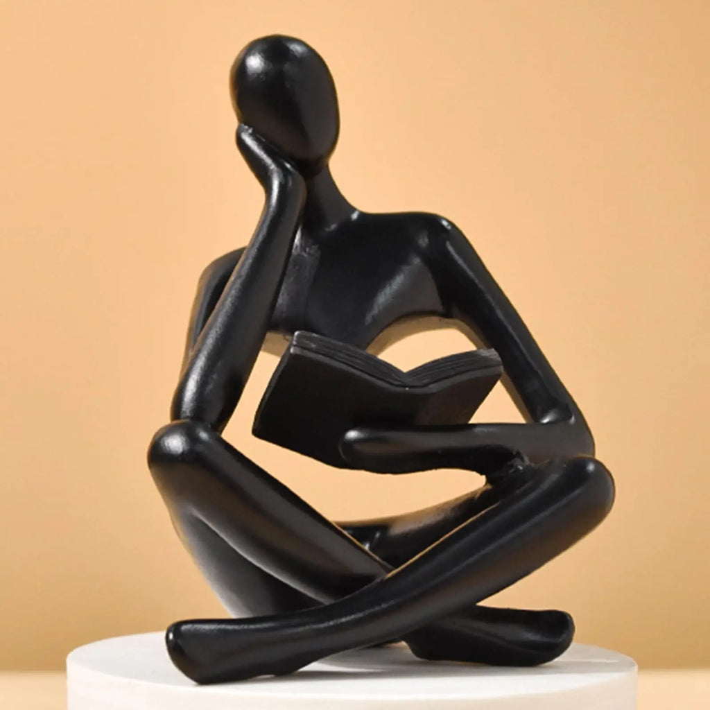 Black Thinker Reading Sculpture sitting with a book on a beige background