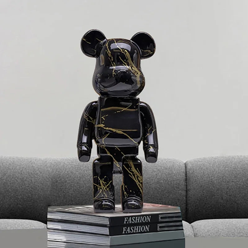 Black and gold marbled graffiti bear figurine on a stack of 'FASHION' books with a gray sofa background