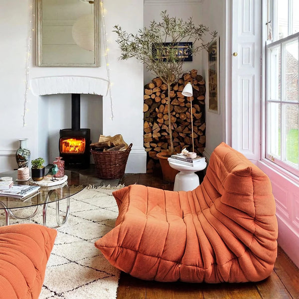 Cozy living room with Orange Corduroy Caterpillar Lazy Sofa, fireplace, and wooden logs.