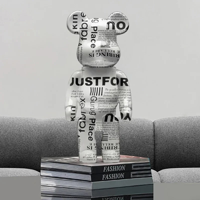 Graffiti bear figurine with newspaper design on a stack of fashion magazines with a gray sofa background