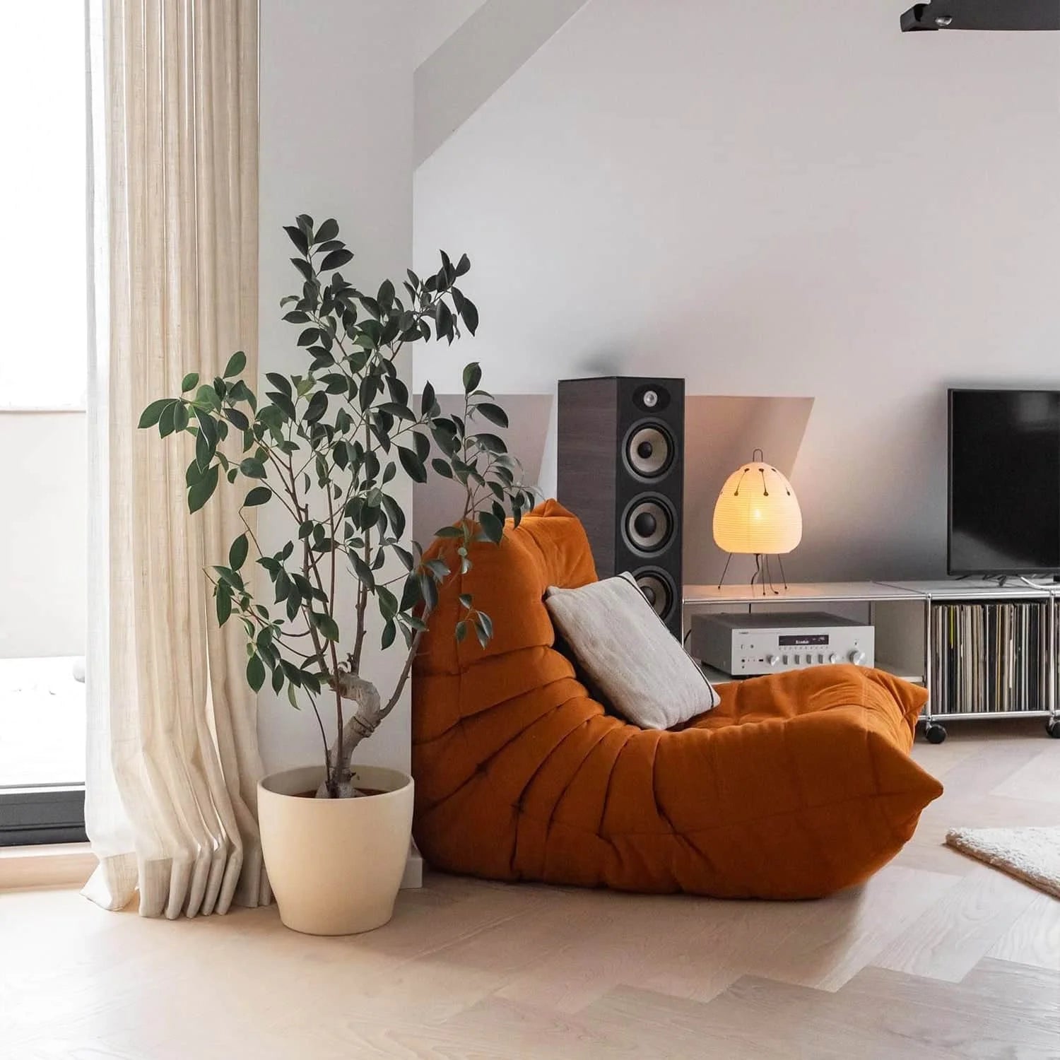 Modern living room with a one seater Orange Corduroy Caterpillar Lazy Sofa, plant, and entertainment setup.