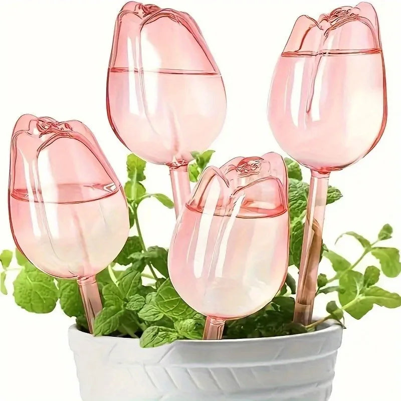 Set of four pink tulip-shaped plant watering globes with green plants inside on a white background