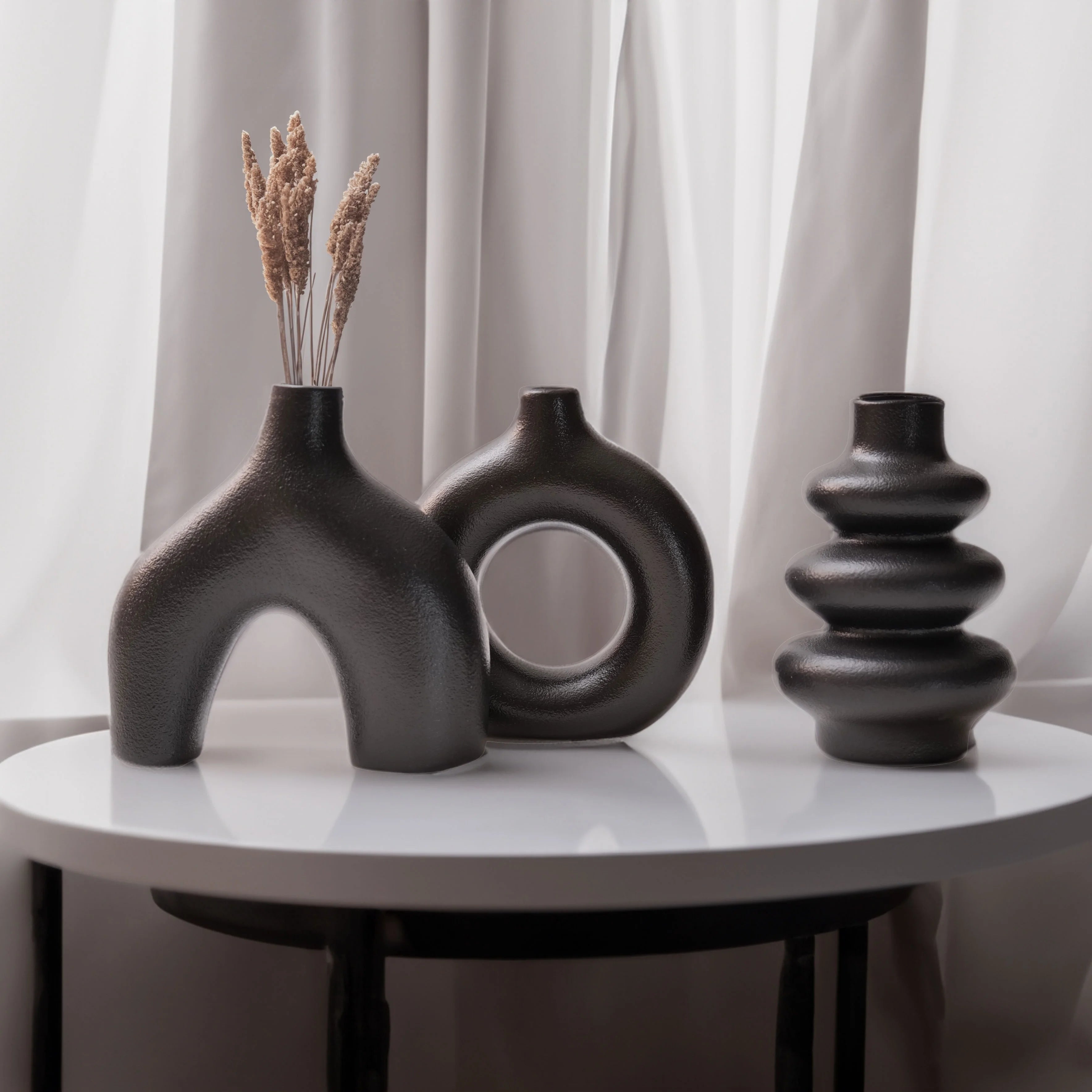 Three black Boho Ceramic Vases on a white table with light gray curtains in the background