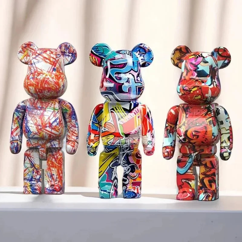 Three colorful, graffiti-style bear figurines on a white surface with a light-colored curtain background.