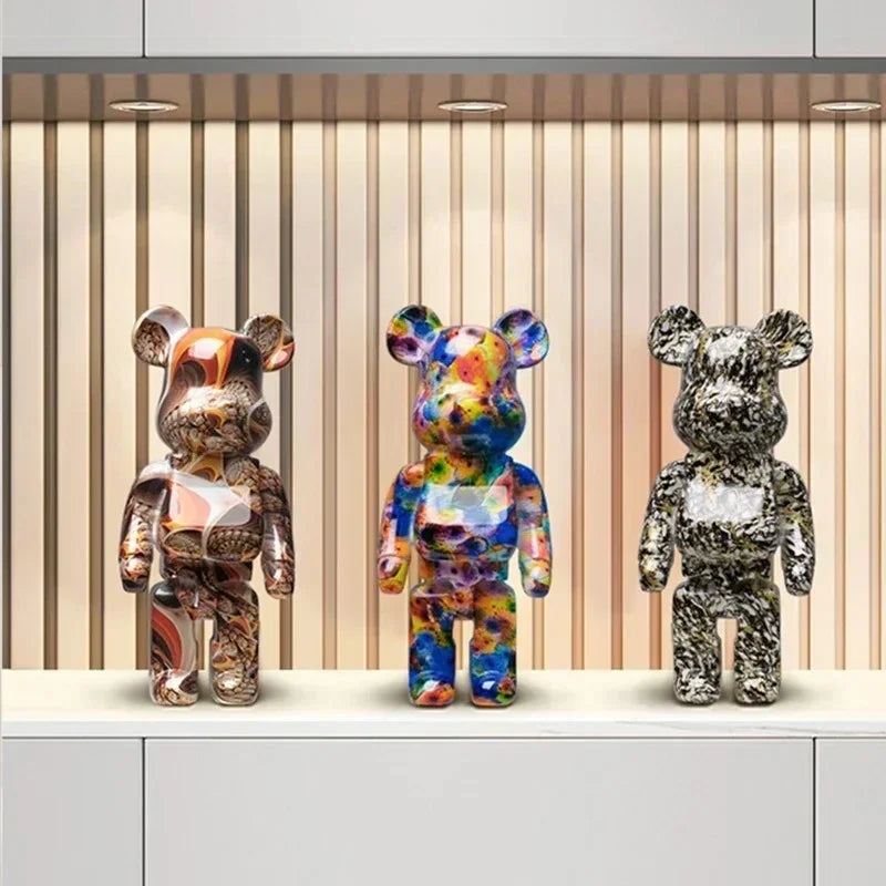Three colorful graffiti bear figurines on a shelf with a striped wall in the background
