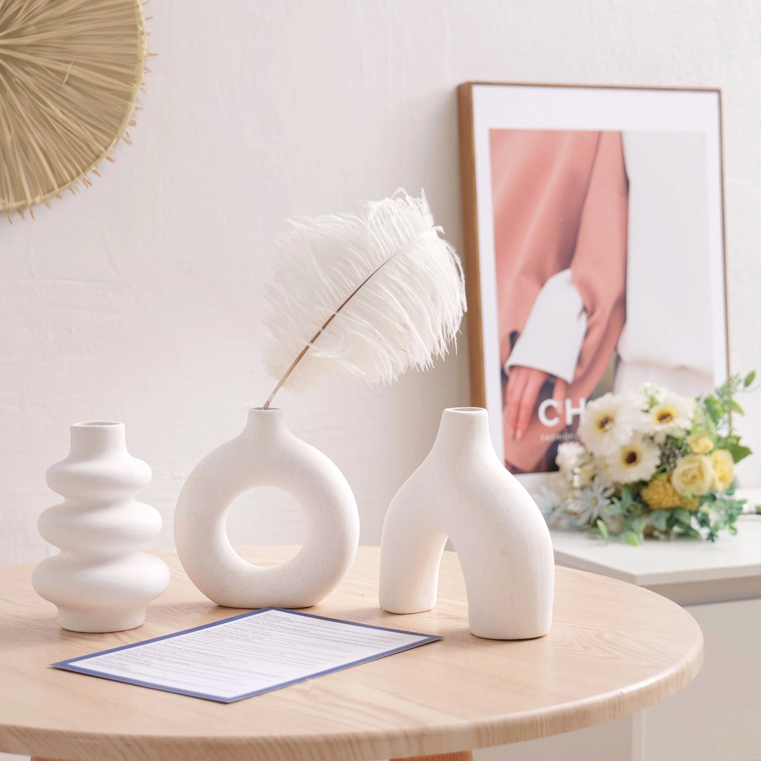 Three white Boho Ceramic Vases on a wooden table with a decorative frame and flowers in the background.