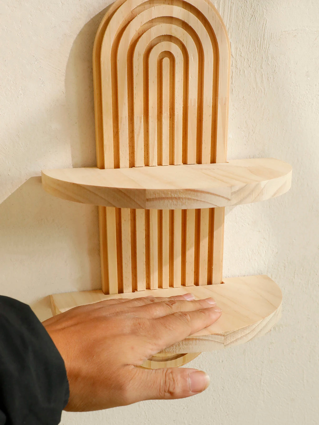 Two tier Boho Wooden Floating Wall Shelf against a beige wall with a hand touching it