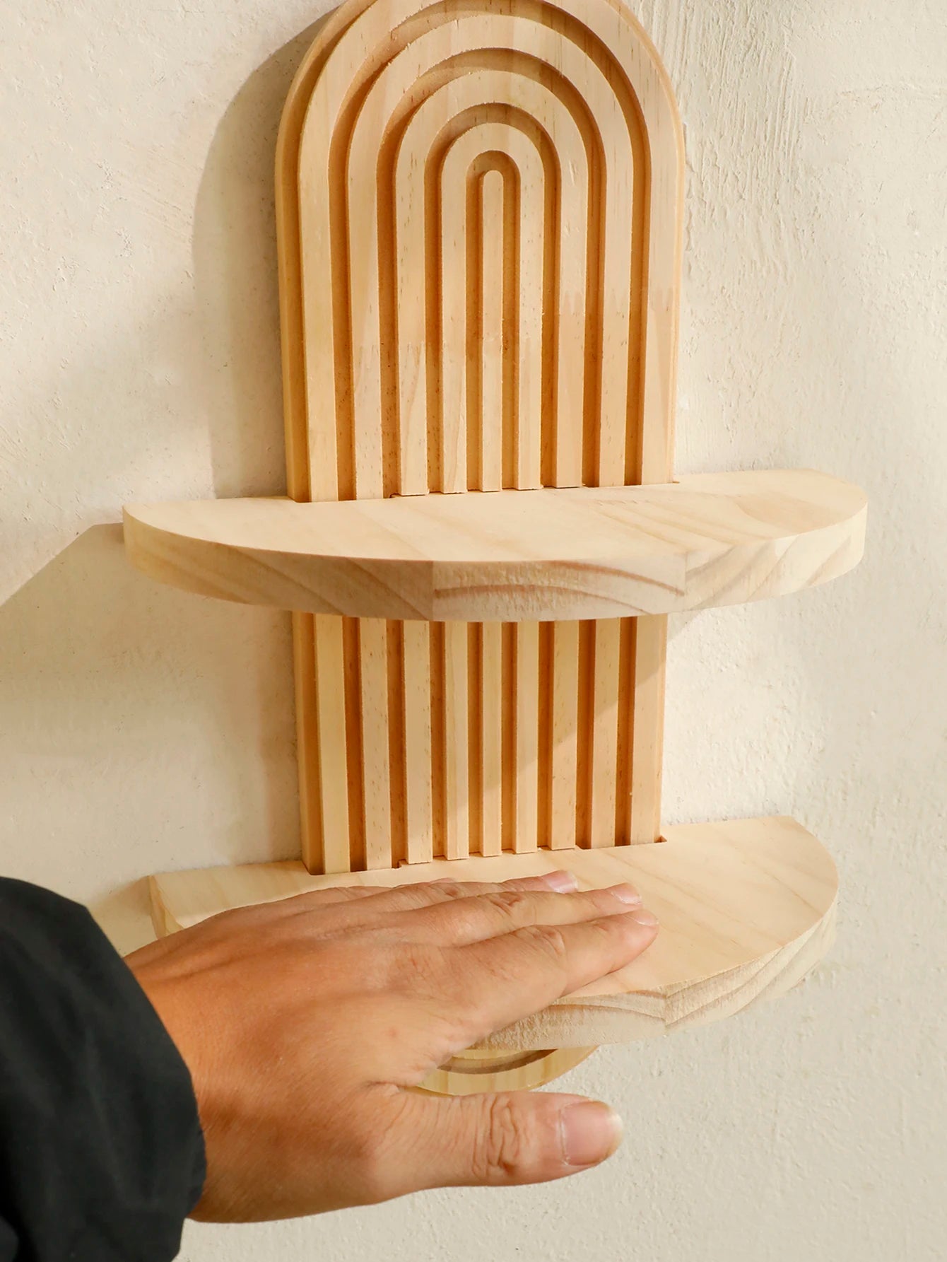 Two tier Boho Wooden Floating Wall Shelf against a beige wall with a hand touching it