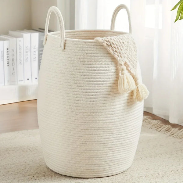 White Boho Cotton Rope Storage Basket with a tassel on a light wooden floor.
