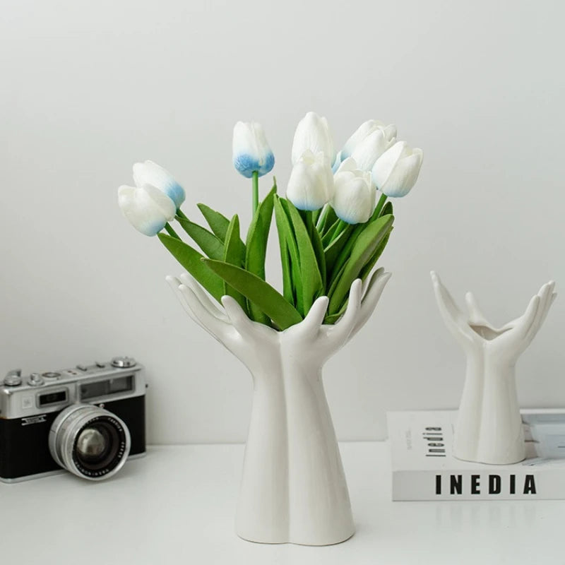 White Ceramic Hand Shaped Vases holding tulips with a camera and book in the background.