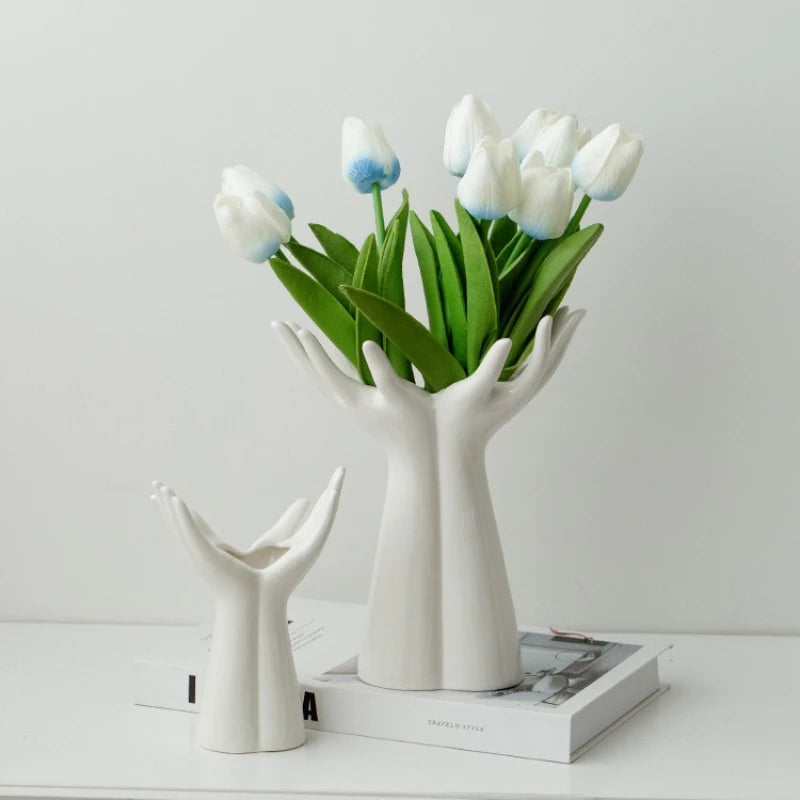 White Ceramic Hand Shaped Vases holding white tulips on a white surface with a light gray background