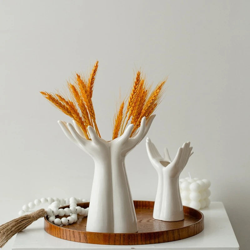 White ceramic hand-shaped vases with dried wheat on a wooden tray against a light gray background